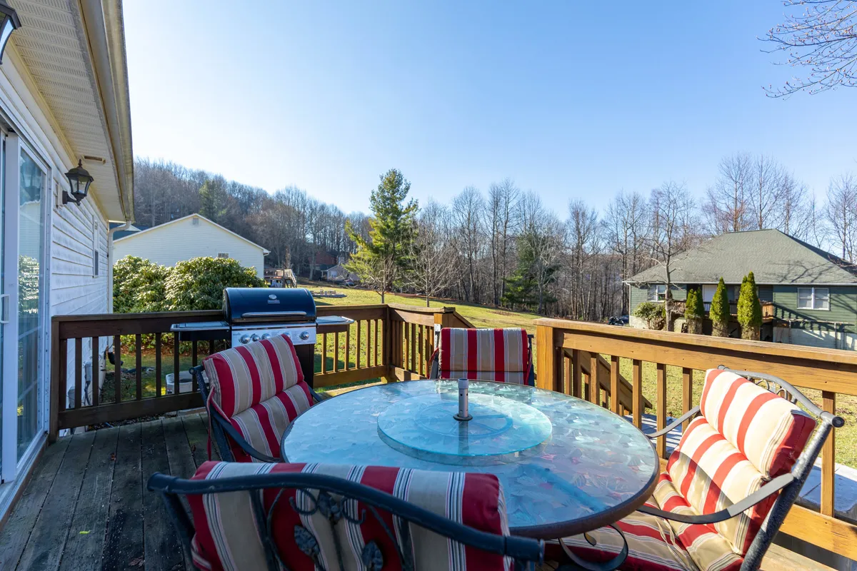 The photo features an inviting outdoor dining setup with a glass table, striped chairs, and a grill, all set amidst a lush green landscape. The atmosphere is cheerful, capturing the spirit of al fresco meals, cookouts, and relaxed gatherings under the sky.