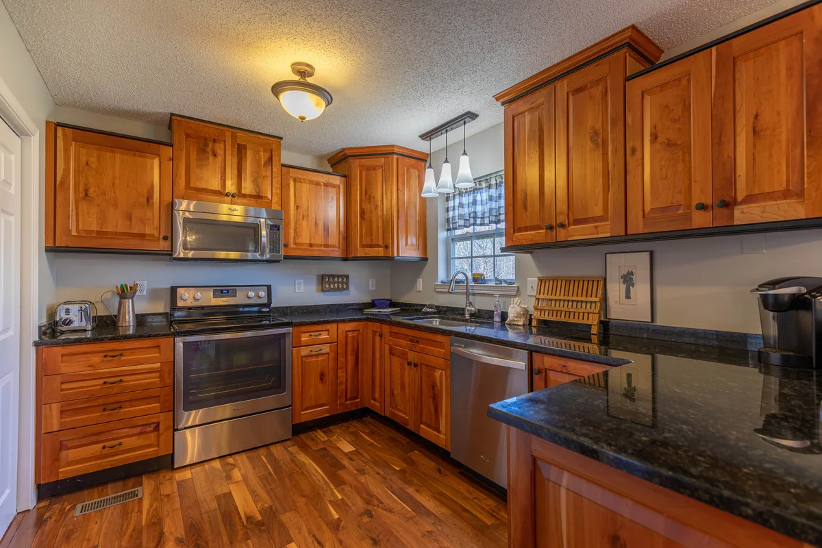 This image highlights a chef-ready kitchen with warm wooden cabinetry, sleek black granite countertops, stainless steel appliances, and a spacious kitchen island. It radiates hospitality and is perfectly equipped for preparing family feasts or casual snacks.