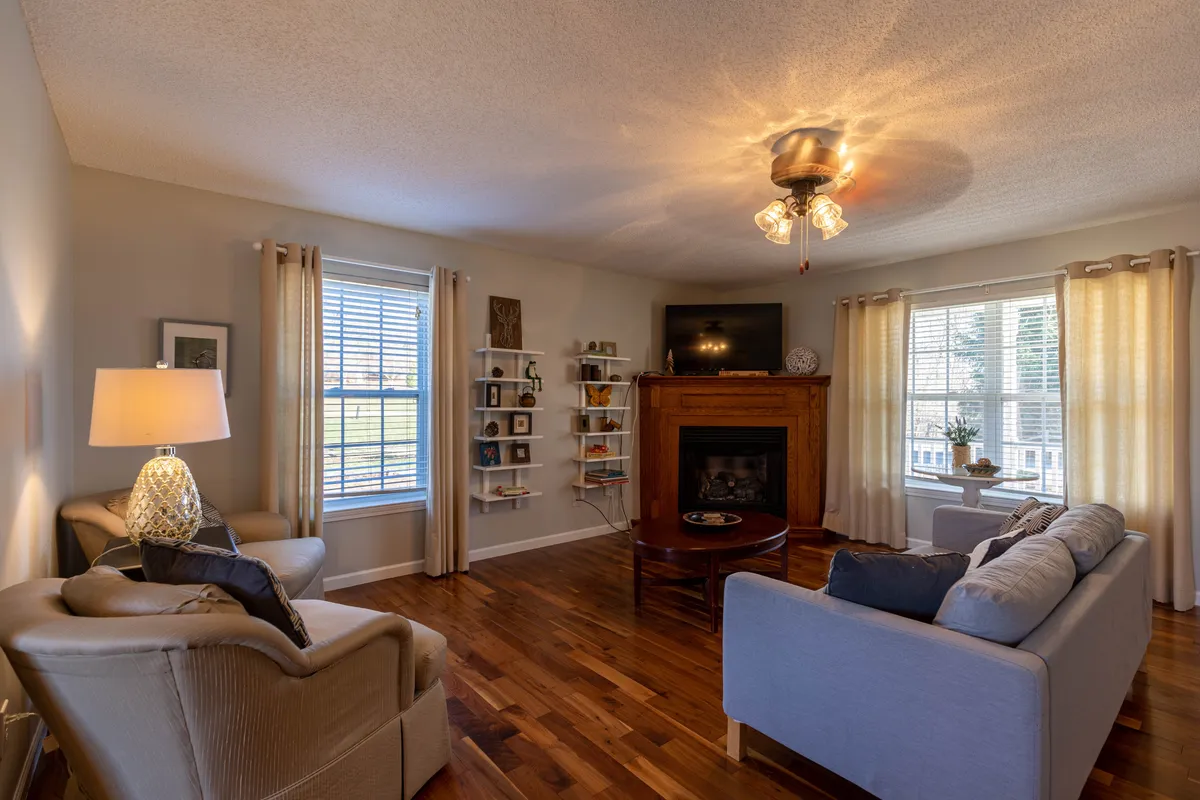 This image captures a warm, inviting living room with a plush sofa, a glowing gas fireplace as the focal point, a window letting in natural light, and a bookshelf that adds a homey touch. The space exudes comfort and is perfect for relaxing with family or friends, reading, or enjoying a cozy night by the fire.
