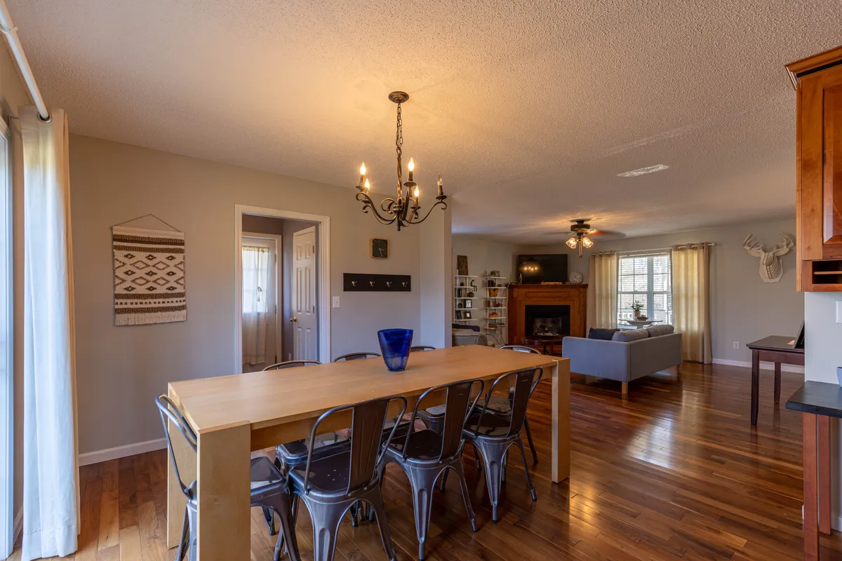 A spacious, elegant dining room featuring a long wooden table set beneath a chandelier, a cozy fireplace, and bookshelves lining the wall. The room invites both intimate gatherings and cheerful family meals, with a focus on warmth and togetherness.