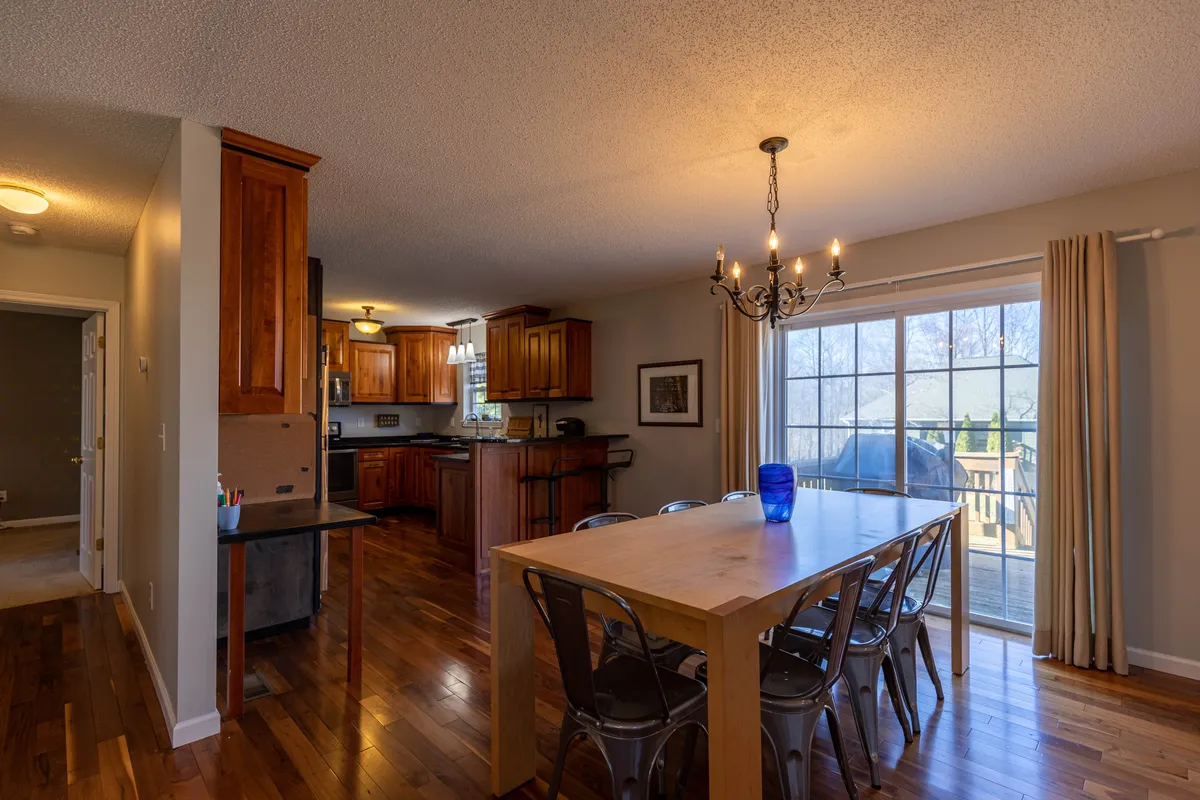 A sunlit wooden dining table under a chandelier, set beside a large window that lets in natural light. The table is ready for family meals or group gatherings, evoking warmth and togetherness.