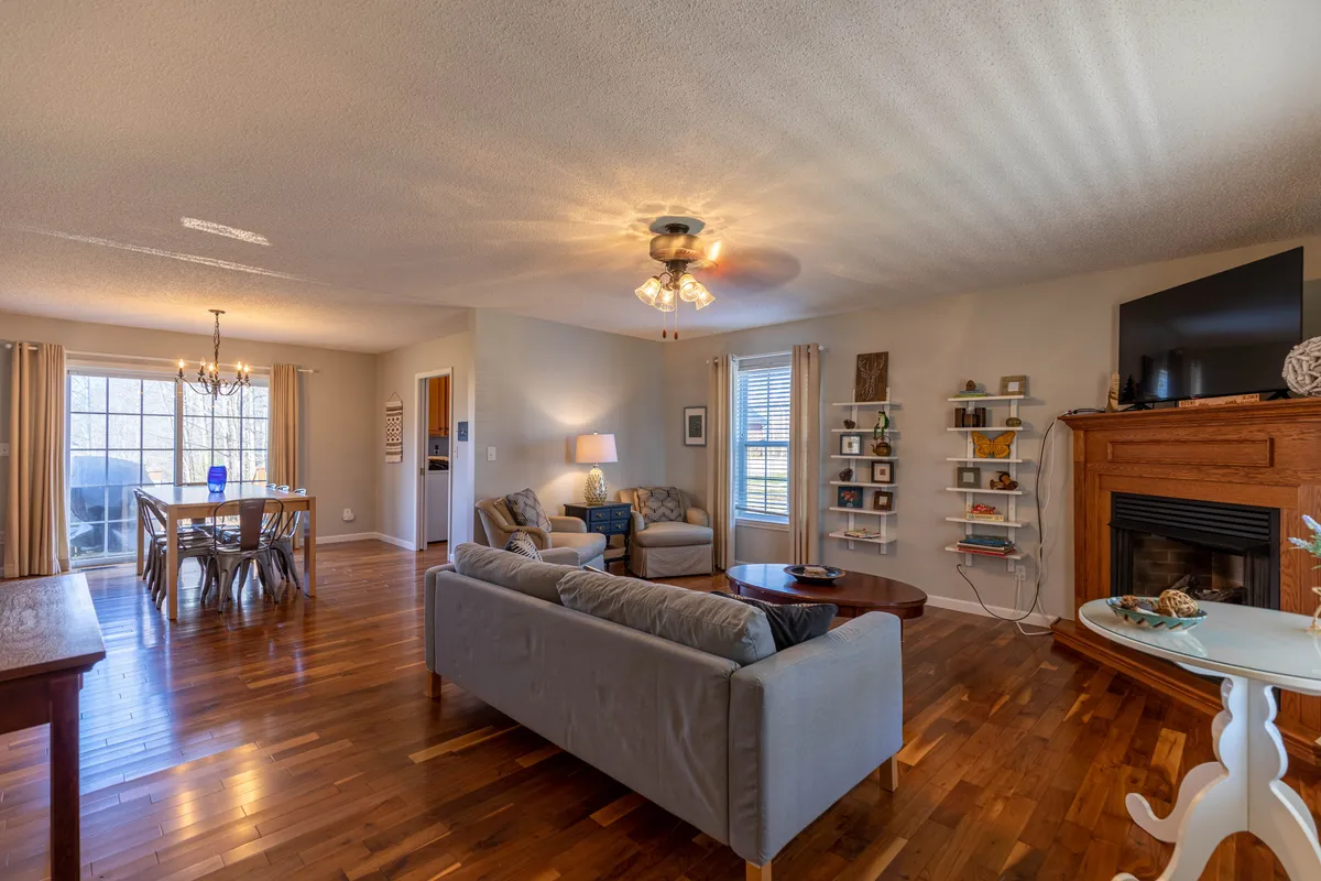 This image offers a broader view of the open-plan communal area, showing a comfy sofa, a sizable dining table, the fireplace, and shelving. The setup is ideal for family gatherings, game nights, and intimate meals, creating a seamless flow between living and dining spaces.