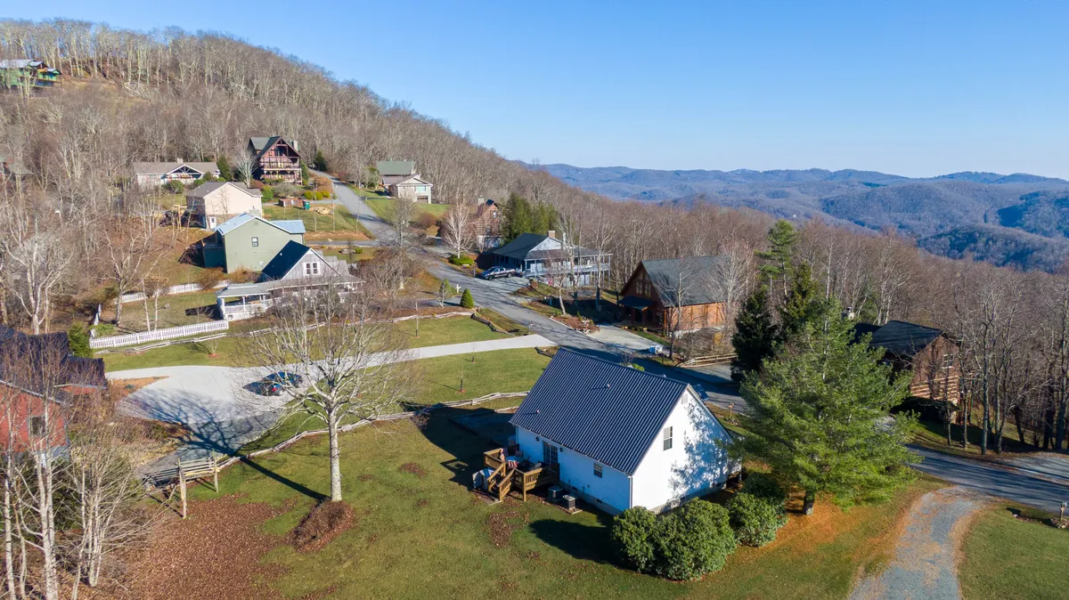 This image showcases a spacious, verdant lawn surrounded by wooden houses, with panoramic mountain views and an open sky above. The tranquil setting is ideal for outdoor activities, family gatherings, and stargazing in the evenings.