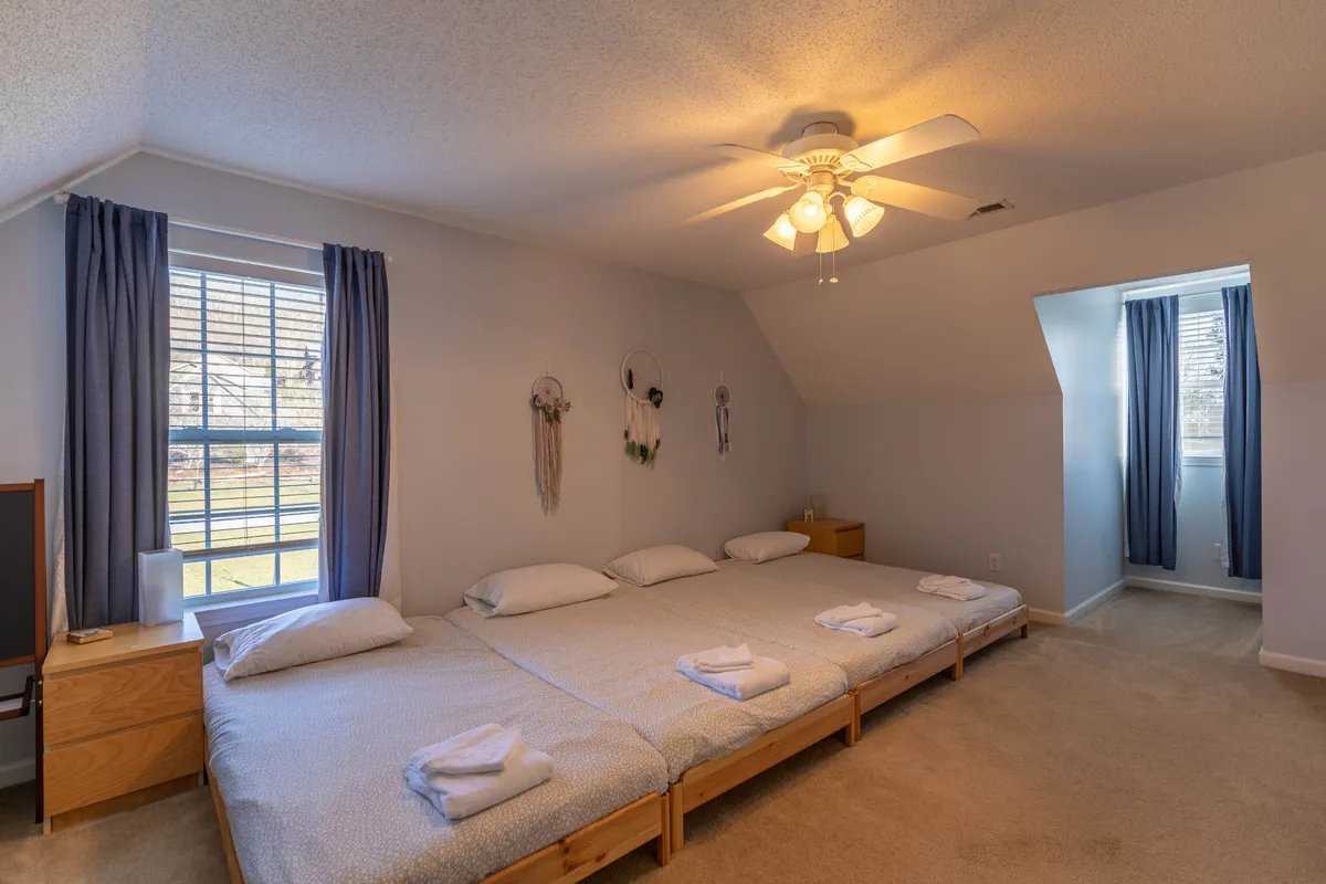 This image showcases a bright, welcoming bedroom with large beds neatly made up, towels carefully arranged, natural light pouring in from the window, and decorative wall art adding a homely touch. The space radiates comfort, cleanliness, and attention to detail.